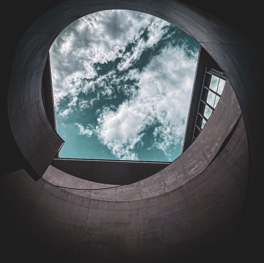 a photo looking up at the sky from the bottom of a cylinder. there are some nice fluffy clouds in a green-blue sky. the rest of the photo is black and white.