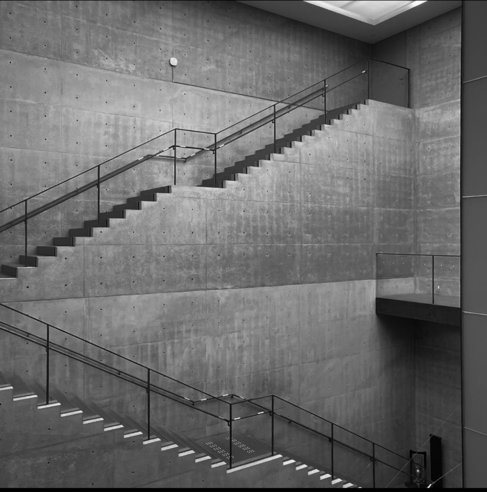 a black and white photo of two sets of stairs along the opposite wall. it’s all concrete and glass, but the architect is tadao ando so it’s merely brutalist-adjacent 