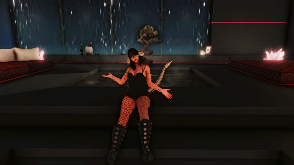 a dark haired auri girl poses on the top of some short steps. Behind her are a pair of lounging beds which flank a central hot tub