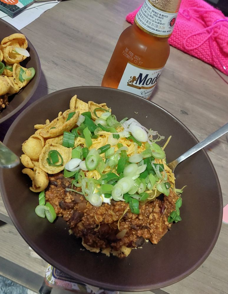 Photo of a brown plate with chili in it with all the fixings and a chilled modelo