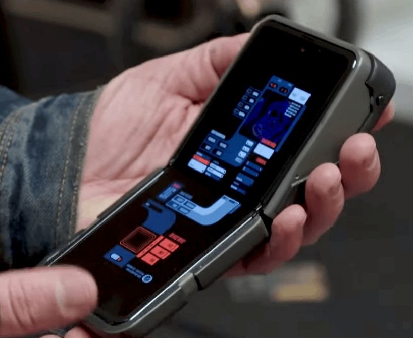 In einer Hand liegt ein aufgeklapptes Smartphone. Auf dem Display sind blau rot leuchtende Bedienelemente im futuristischen Stil. Das Gehäuse ist etwas aufgemotzt mit grauen Erweiterungen.