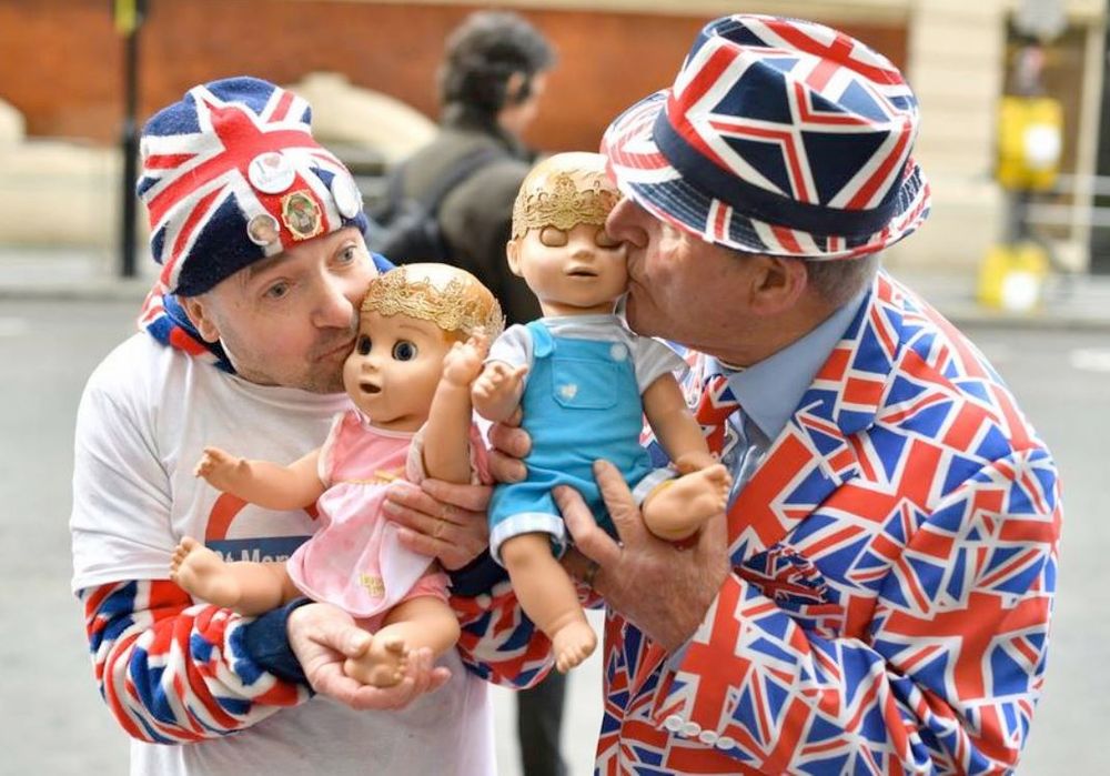 Photo of two absolute twits, head-to-toe in union jack clothes, kissing dolls dressed as the british royal family babies. the one on the right looks suspiciously like keir starmer, but he only hopes it's him. 