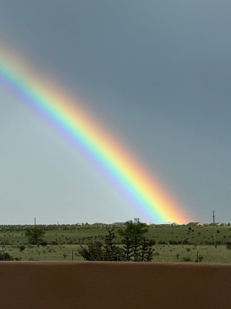 An intense rainbow viewed over a stucco wall.
