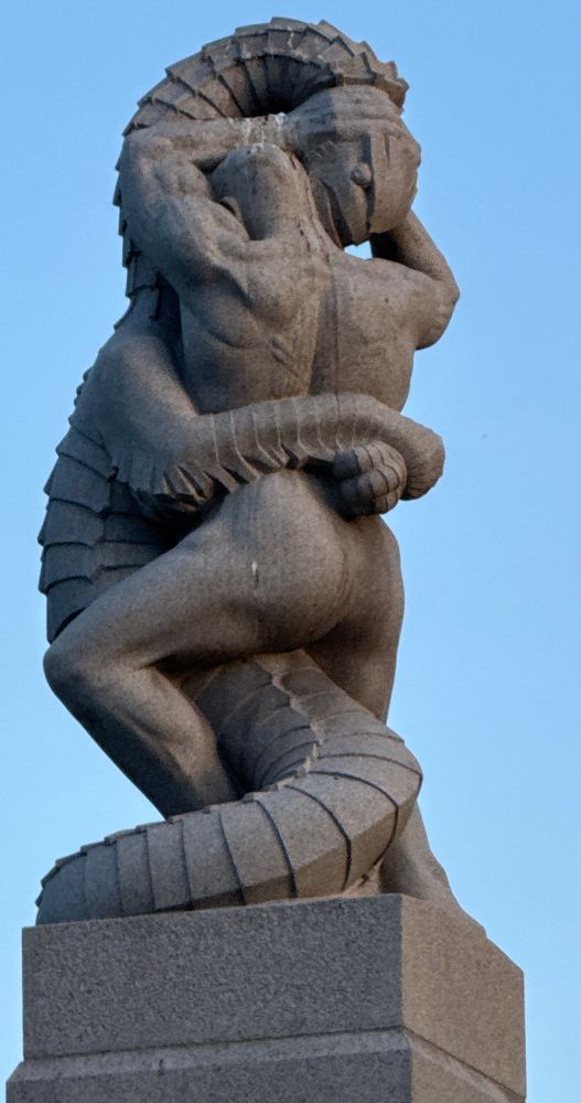 A nude man clutches a fish person’s head. The fish appears to be into it. 