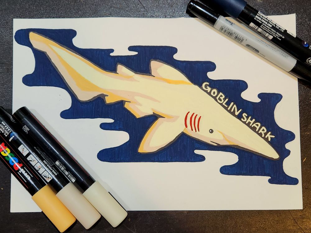 An acrylic marker illustration of a pale goblin shark with red gills against deep blue to help it stand out against the white paper. There are 4 posca markers (ivory, beige, apricot, & navy blue) as well as a black copic. The text says Goblin Shark.