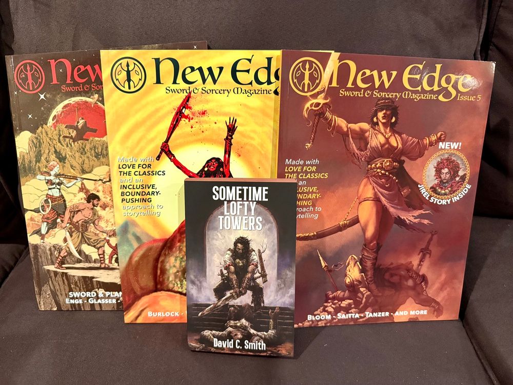 Issues 5, 6, and 7 of New Edge Sword & Sorcery Magazine propped against couch cushions, with the paperback for David C. Smith’s SOMETIME LOFTY TOWERS in front.