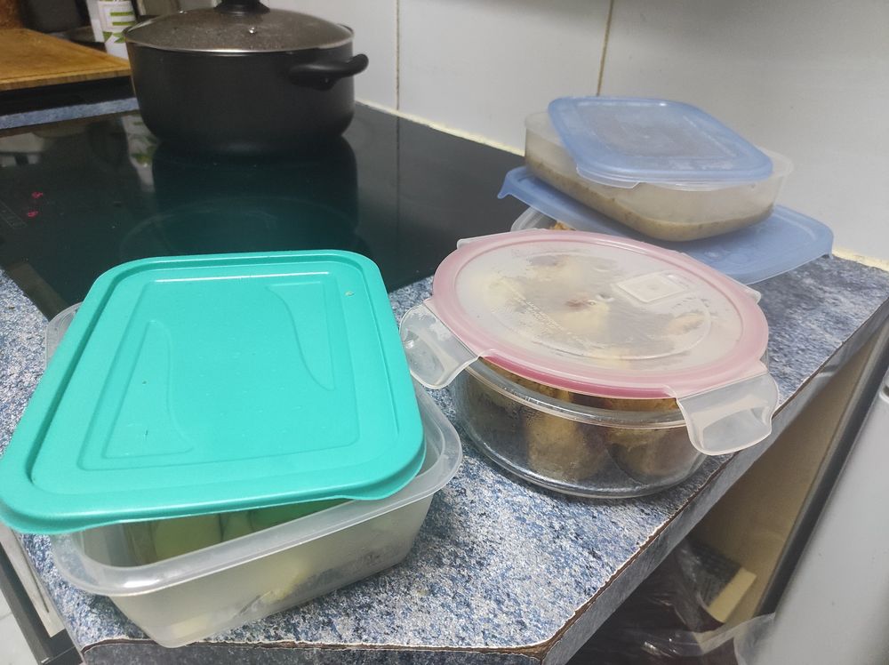 Foto de la encimera de mi cocina, con varios tuppers llenos de comida. De fondo hay una olla en la que te hecho salsa de tomate y gambas.