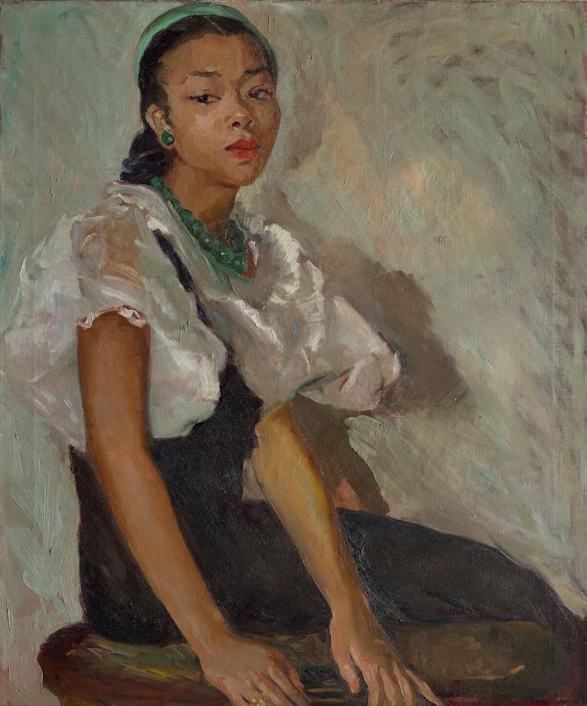 A portrait of a young black woman, seated, green cap and green necklace, transparent white cowl over black dress.