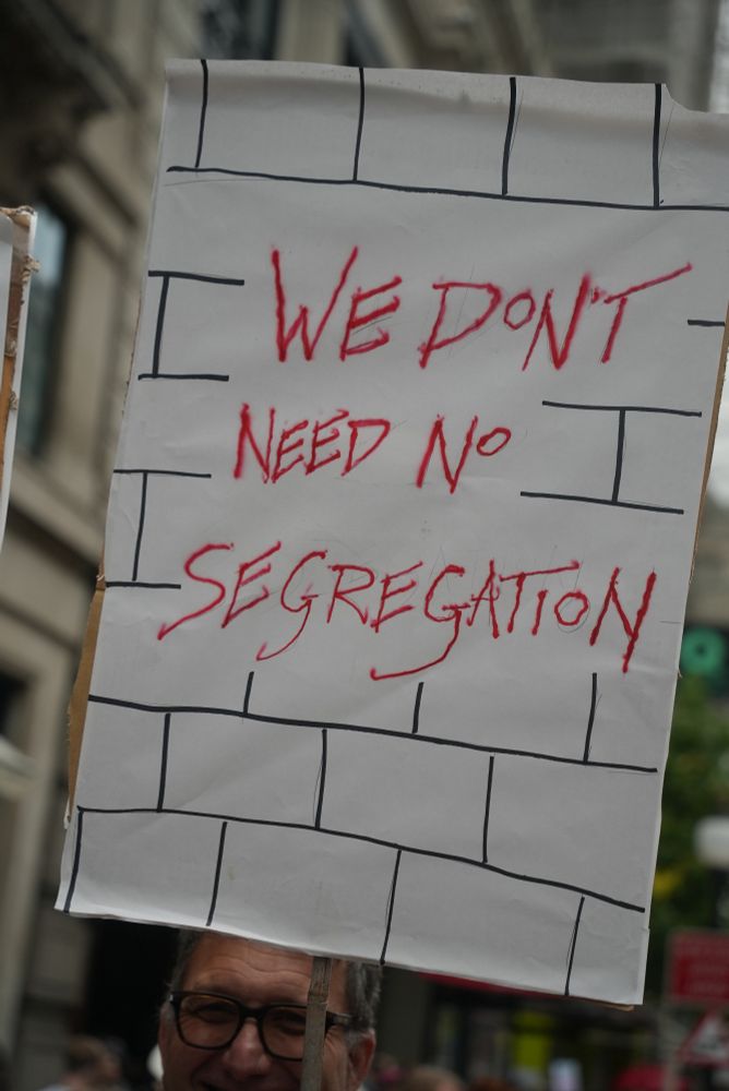 A protest sign that says "We don't need no segregation" written over a hand drawn brick wall texture.