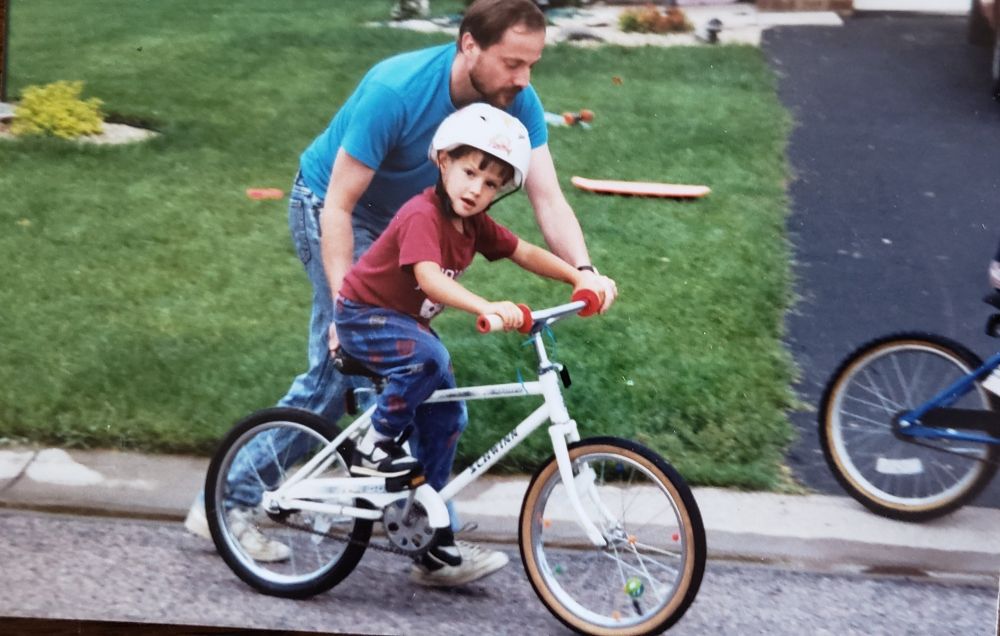 A man in a blue shirt pushes a boy on a white bike