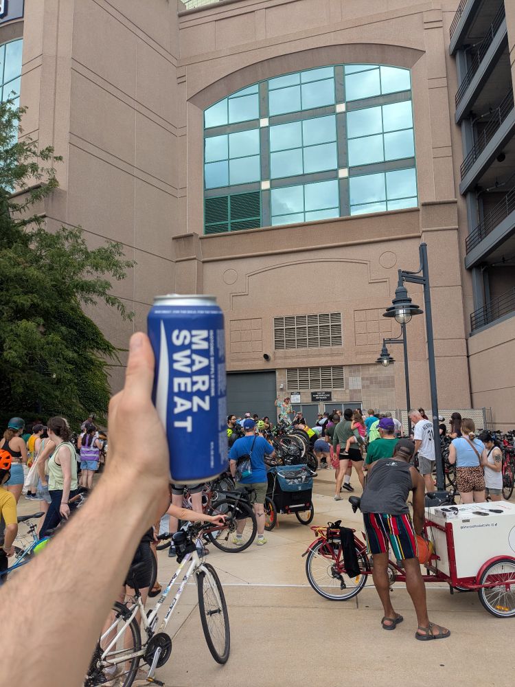 Me holding a can of Marz sweat in front of a group of cyclists listening to an organizer talk about Bike Sox