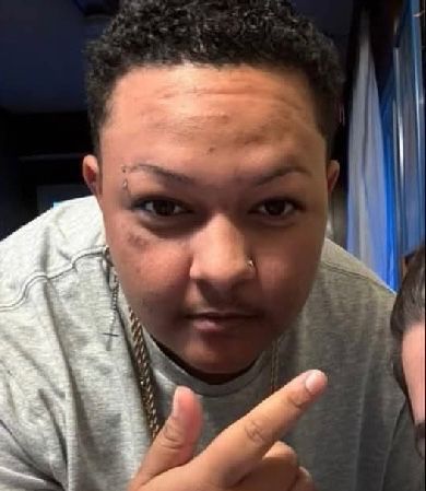 A photo of Sam Nordquist, a biracial (black and white) trans man. He has short curly hair and visible stubble on his upper lip.