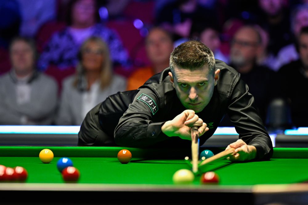 Mark Selby plays a shot on a snooker table with a rest.