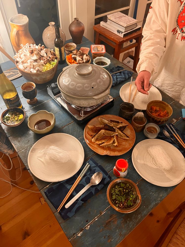 A table set with ceramic plates, bowls, small dishes with hot pot.