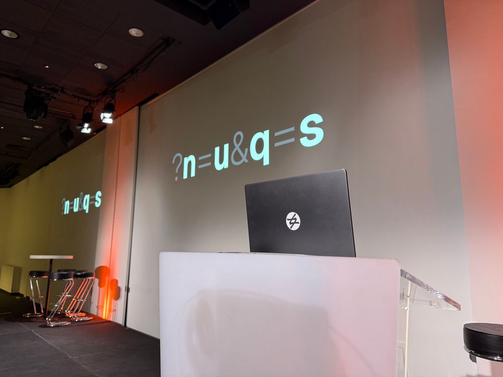A conference podium with a laptop on top, and the slides on the back show the nuqs logo.