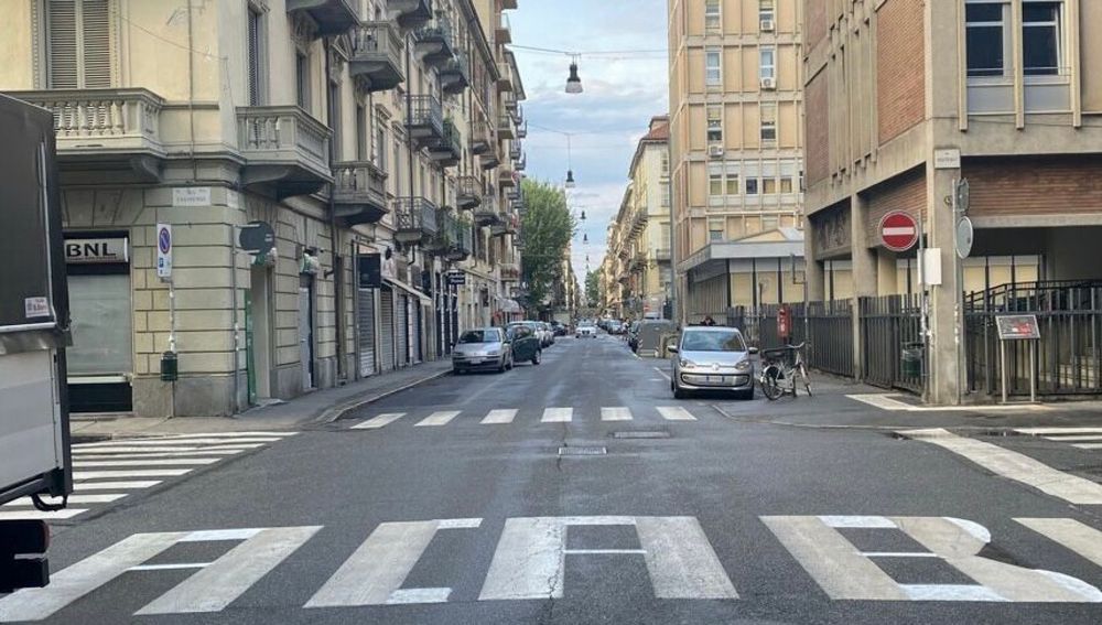 Eine urbane Straßenansicht zwischen mehrstöckigen Wohn- und Bürogebäuden. Autos sind am Straßenrand geparkt, ein Fahrrad steht rechts an einem Zaun. Im Vordergrund ist ein Zebrastreifen zu sehen, der durch leichte Ergänzungen mit weisser Farbe  den Schrifzug "ACAB“ ergibt. Der Himmel ist leicht bewölkt, und die Straße wirkt relativ leer.