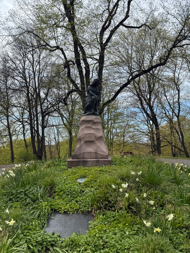 A park statue of a forlorn woman named Linda. She is surrounded by trees, lush grass and spring blooms.