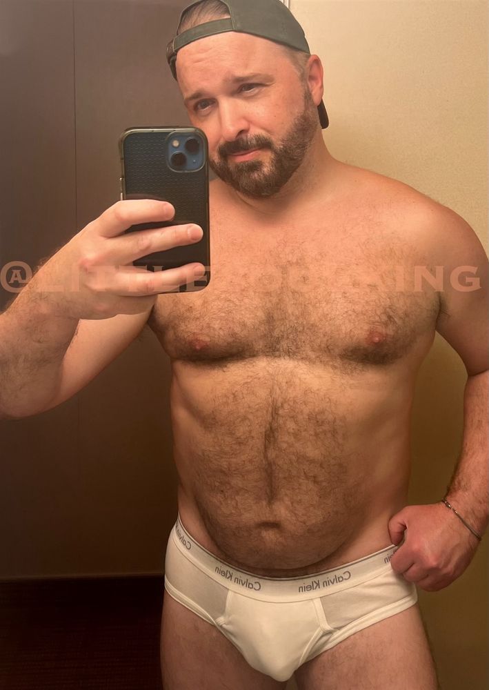 A mirror selfie of a furry, bearded man. I am wearing only a backwards green ball cap and white Calvin Klein briefs.