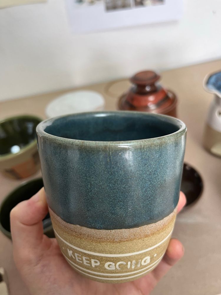 Small cup with a teal glaze, with the words “keep going” inlaid, albeit not very cleanly 
