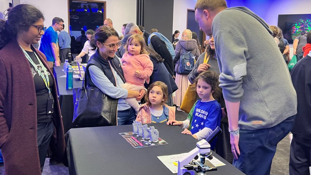 Upasana explaining  to a group of kids and their families the difference between four models of 👌🏾 hands 3D printed at different resolutions in order to explain the importance of resolution in microscopy.