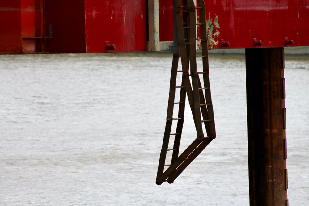 A rusty ladder folded into a triangle hanging from a jack up barge.