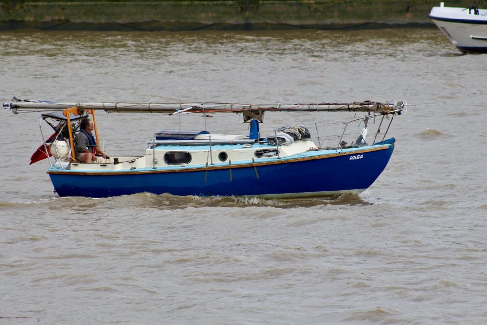 Small blue and white yacht with her mast down so she can pass under the many bridges on the central London tidal Thames.
