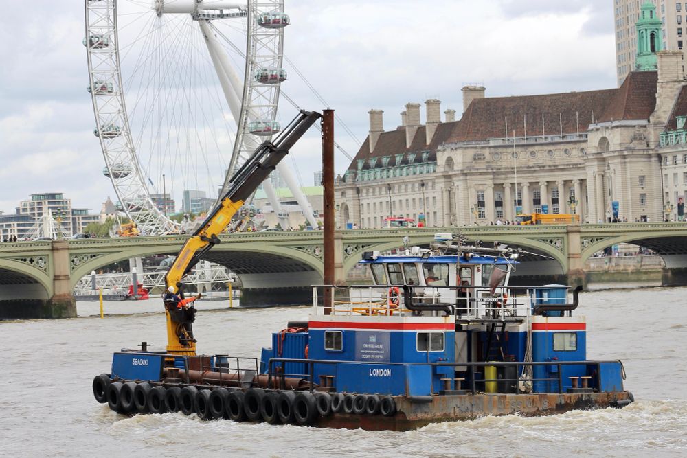 Blue and white multicat, with a red stripe and a yellow crane heading towards Westminster Bridge and the London Eye. She's a serious working vessel. To know more, see https://www.cpbsmarineservices.co.uk/Seadogmulticat