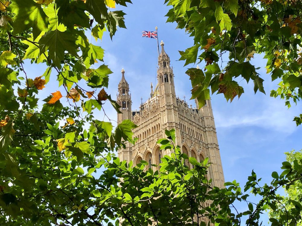 A honey coloured Neo-Gothic tower, with British flag flying, against a blue sky and misty clouds.