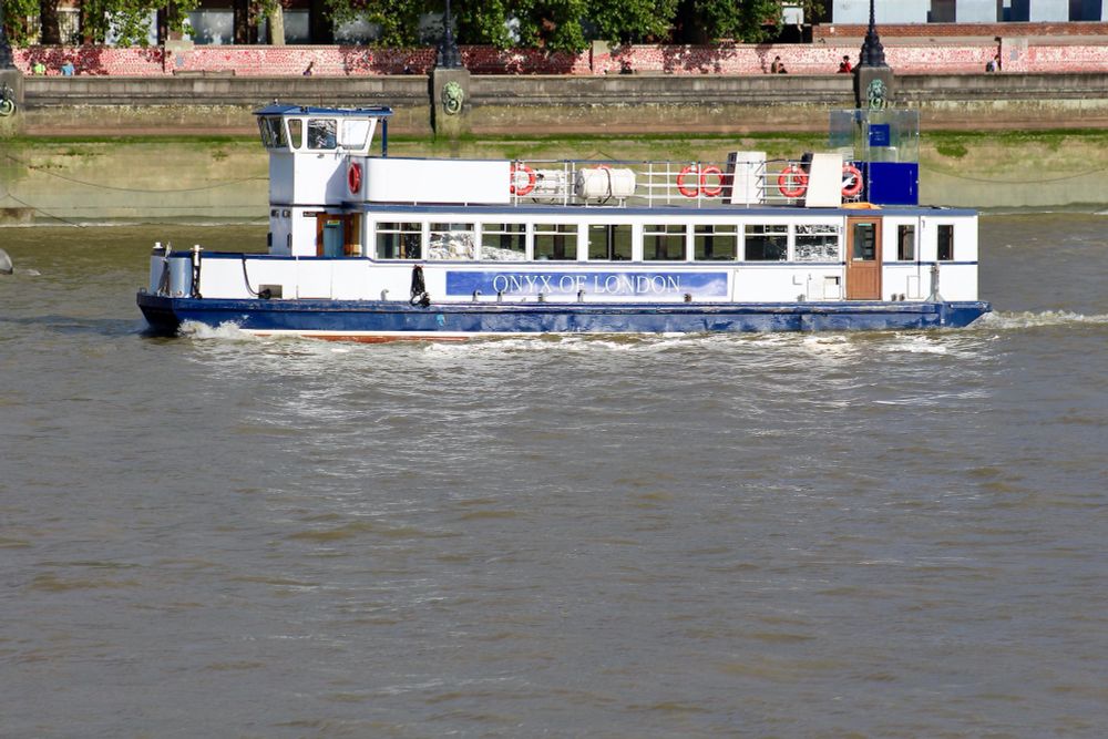 Party boat ONYX OF LONDON sailing on greyish water passing the red hearts on theUK National Covid Memorial Wall.