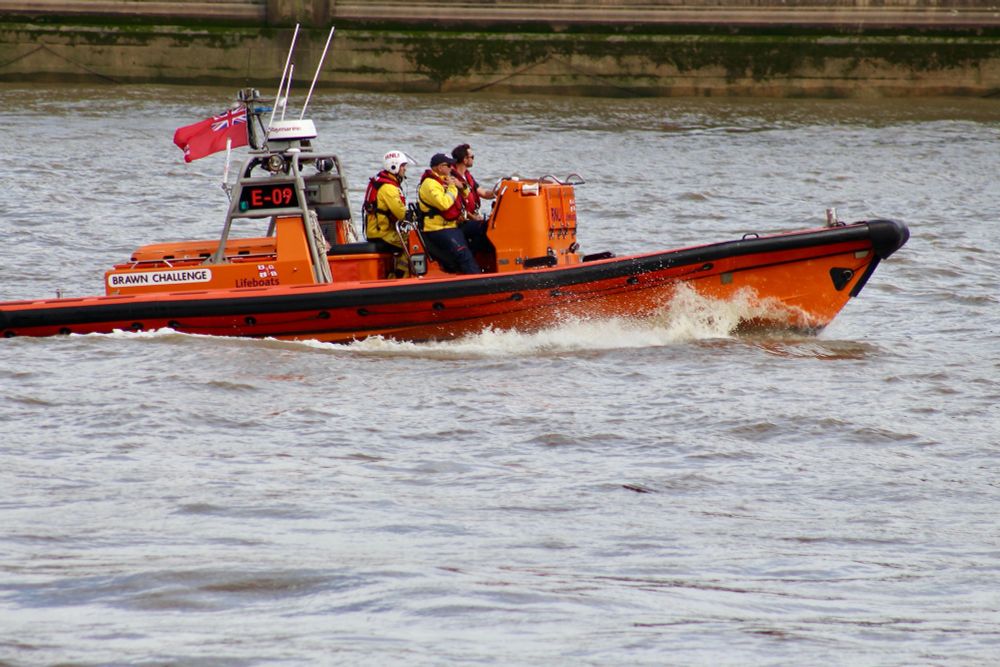 Lifeboat in the distinctive orange colour of the RNLI - Royal National Lifeboat Institution - heading upstream to base at Chiswick, one of four Lifeboat Stations on the tidal River Thames.