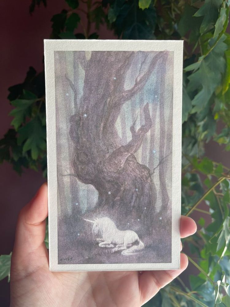 a unicorn rests beneath a large twisted old tree in a forest, surrounded with the glowing lights of fairies which are attracted to the glow of the unicorn. 