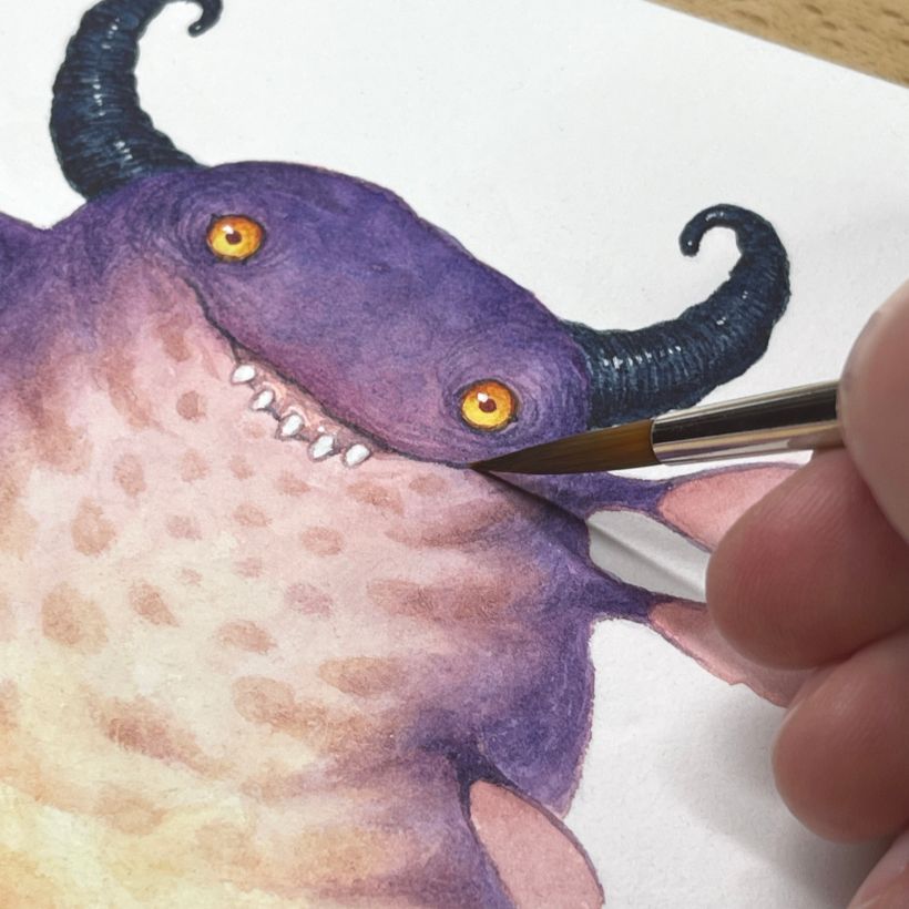 close up of a purple monster with black horns and yellow eyes, my hand is there with the brush painting it