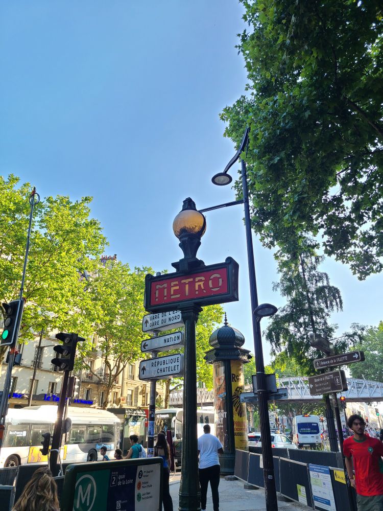 Photograph of a Parisian street. A prominent metro sign can be seen. 