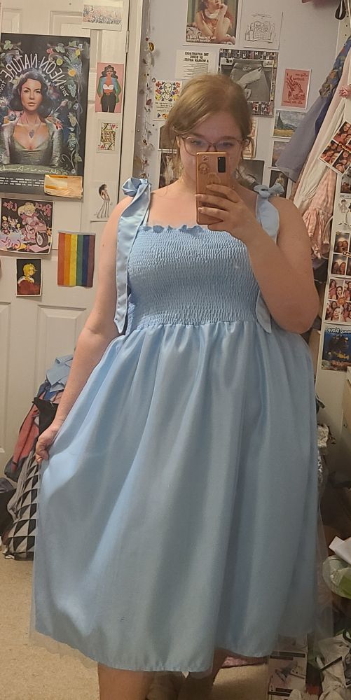 Woman takes a mirror selfie in a long blue dress with a large gathered skirt. 