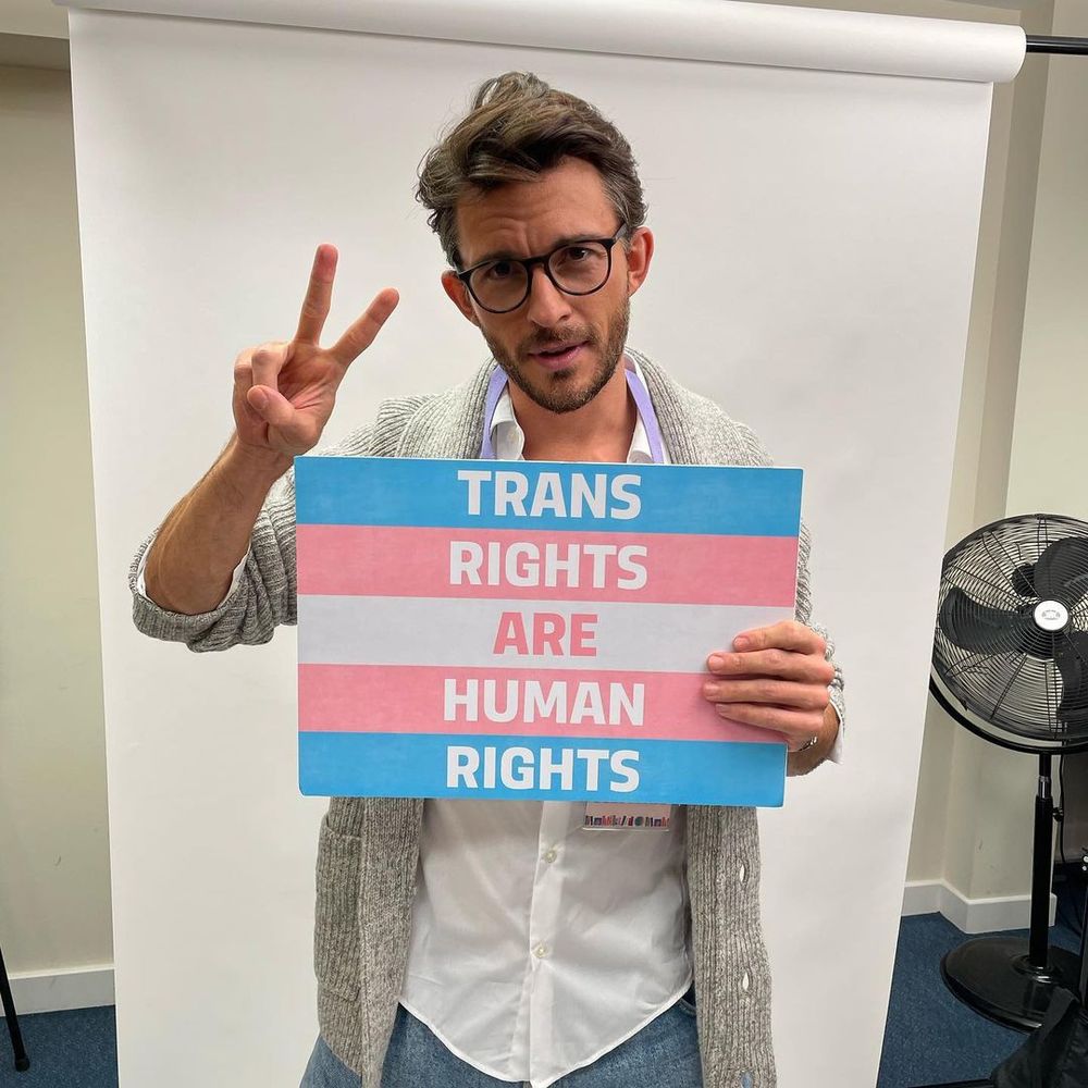 Photo de l'acteur Jonathan Bailey, élu homme le plus sexy 2025 par le magazine People, tenant un panneau "les droits des personnes trans sont des droits humains"