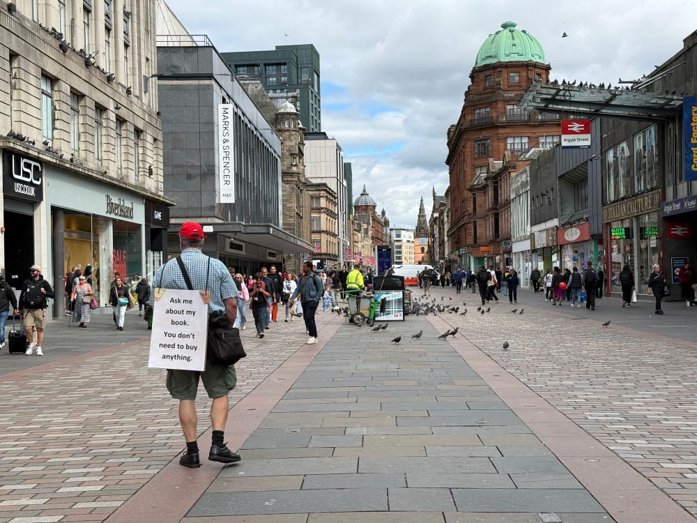 Man wearing a sandwich board that says "Ask me about my book. You don't need to buy anything."
