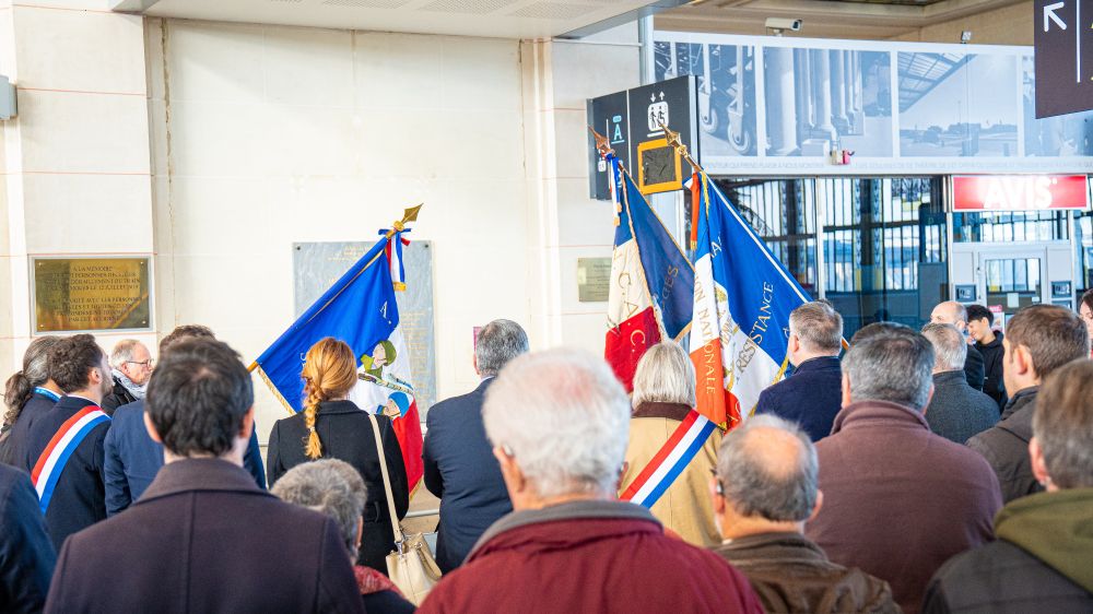 Moment de recueillement lors de la cérémonie du 11 novembre à la gare de Limoges. Écharpes tricolores et drapeaux de l’ANCAC entourent les participants tournés vers les plaques commémoratives des agents SNCF morts pour la France.