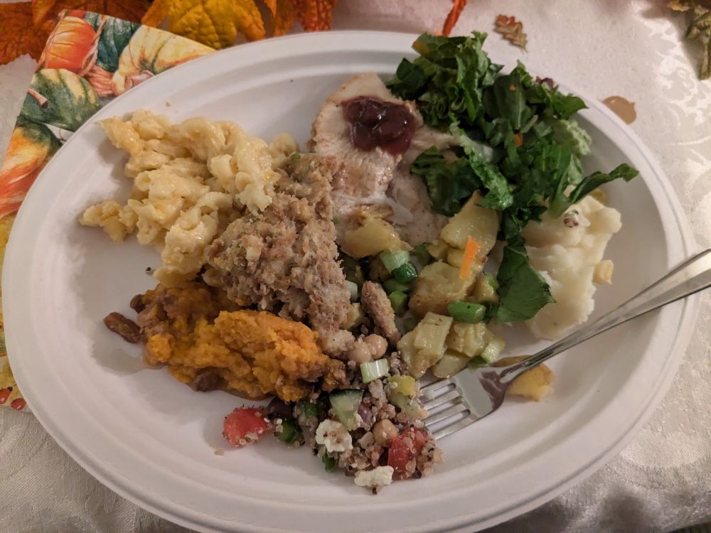 A plate full of thanksgiving food. Turkey with chutney, sweet potatoes, mashed potatoes, stuffing, salad, Mac and cheese. 