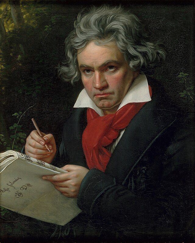Portrait of Ludwig van Beethoven. He is writing the score for his Missa Solemnis, and is wearing a dark coat, wide collared white shirt and a red scarf.