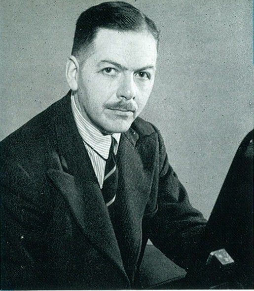 Black and white photograph of composer Victor Hely-Hutchinson. He is wearing a dark suit with a striped tie, and has a thin moustache.