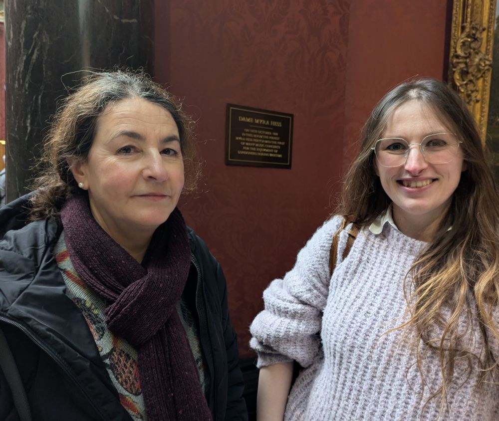 Photograph of Jessica Duchen (left) and Leah Broad (right) in front of the Myra Hess plaque in the National Gallery, London.