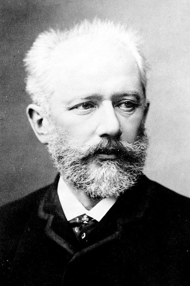 Black and white photograph of Tchaikovsky. He is wearing a dark jacket, and has thick facial hair despite a receding hairline.