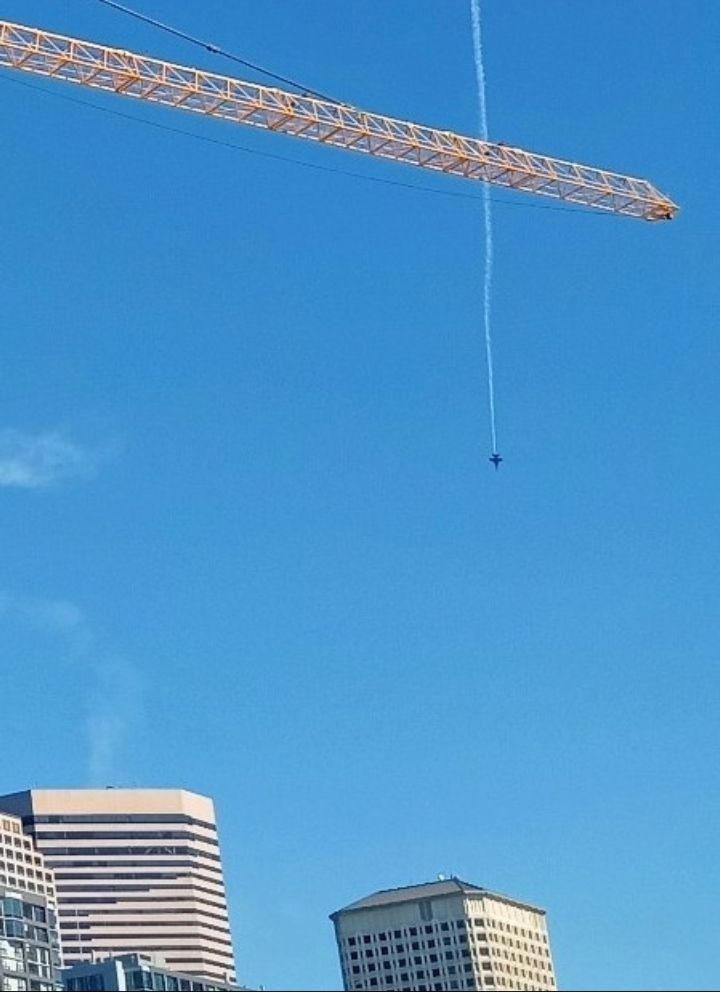 A blue-sky day in Seattle.
August of 2024.

A Navy jet dives straight down above the Emerald City skyline.

The Blue Angels fly Boeing F/A-18 Super Hornets.

They perform annually for Seafair, a summer festival in the Pacific Northwest.

Description:

A yellow industrial crane.at the top of the frame.

A handful of skyscrapers at the bottom of the frame.

A white contrail behind the diving jet.

A beautiful day on the Elliott Bay waterfront.