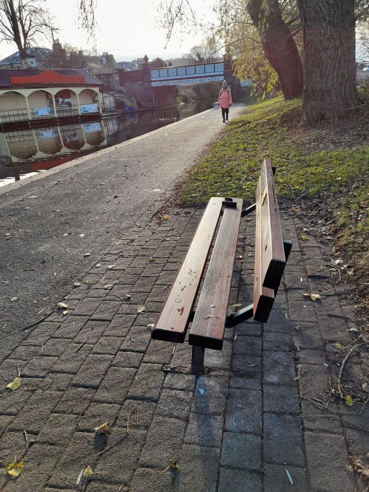 a picture of a restored bench on the path near the canal, with the Ashley Terrace boathouse in the background.