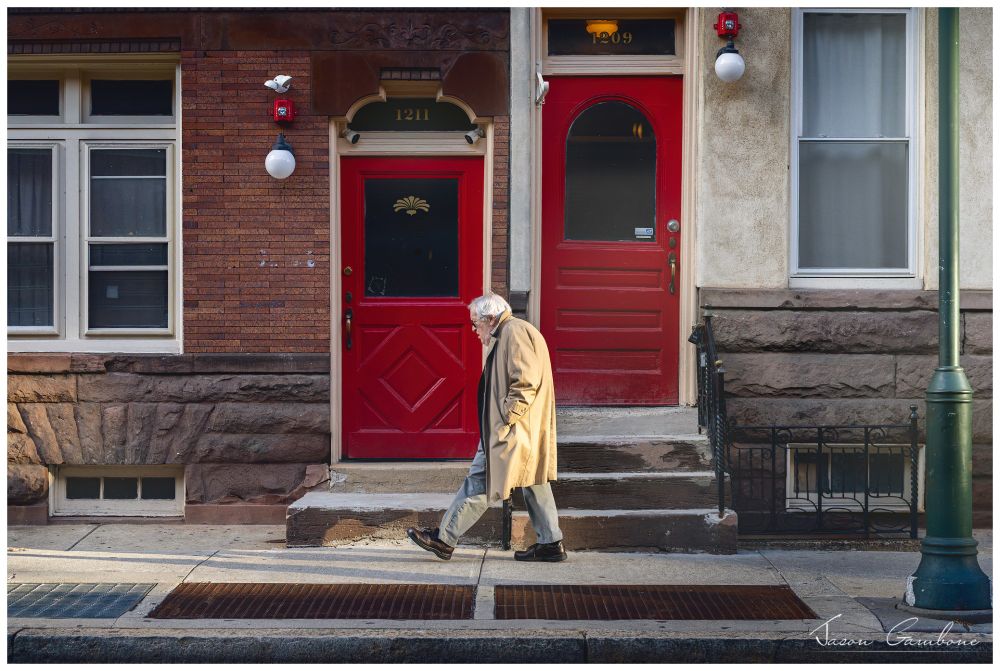 An older gentleman walks in a hurry down the sidewalk.
