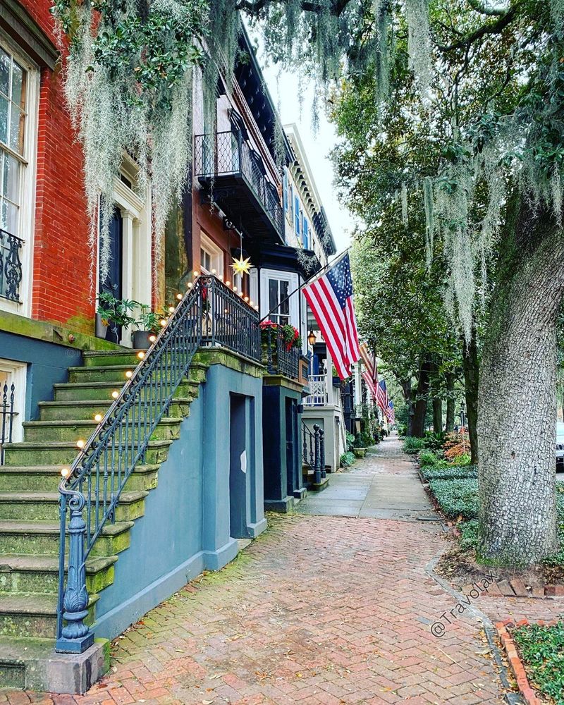 Travel view of Savannah, Georgia, showing moss-draped trees and historic brick houses with American flags.