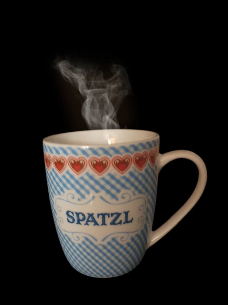 blauweißer Henkelbecher mit roten Herzchen und der Aufschrift SPATZL, aus dem Dampf eines Heißgetränks aufsteigt