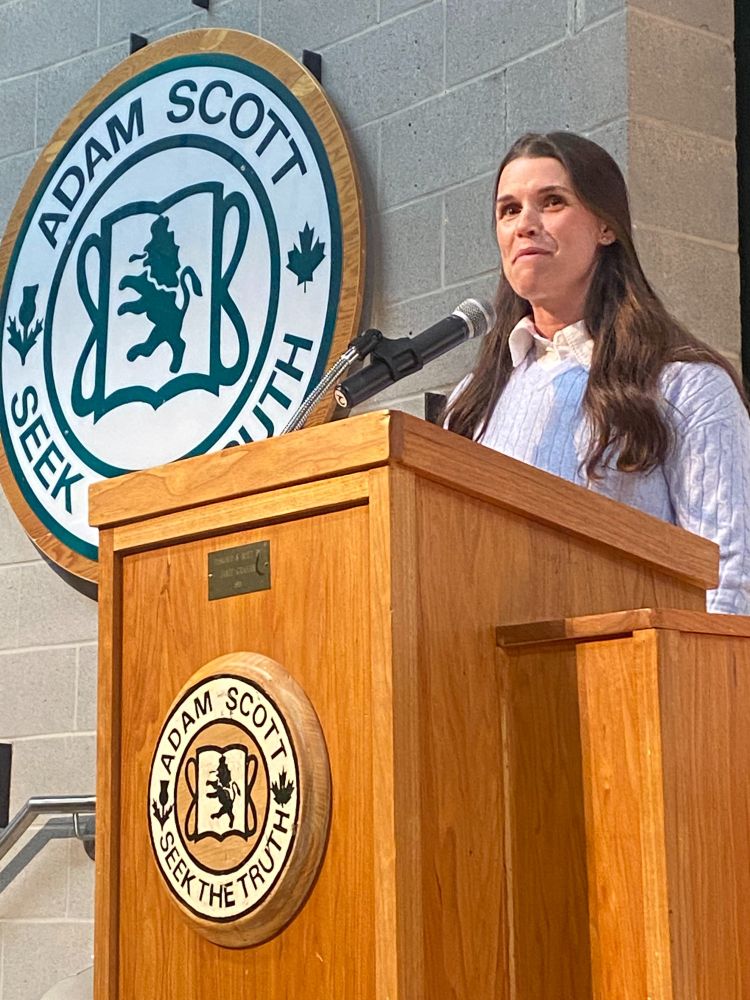 Emma speaks at the podium at Adam Scott school