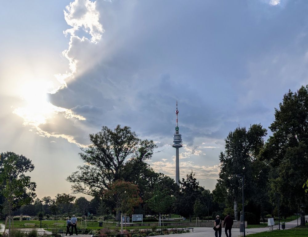 Der Donauturm, über dem eine Regenwolke hängt, im linken Eck zeigt sich aber schon die Sonne.