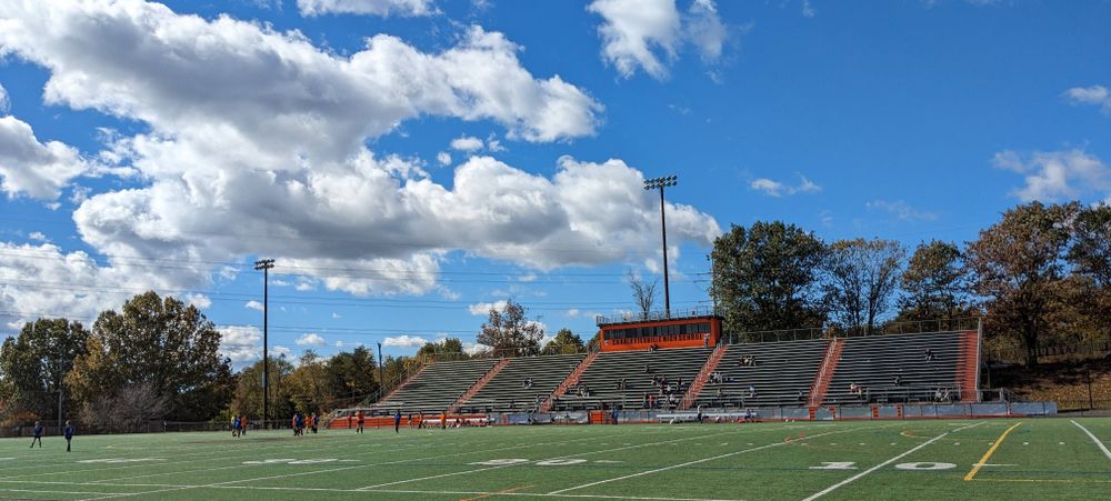 A youth soccer game being played on a high school American football field under a blue sky with some white, fluffy clouds.